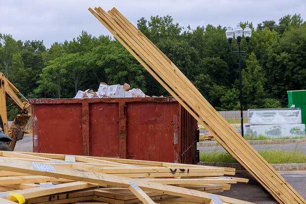 During a house renovation in White Plains, NY, construction trash and garbage fill multiple dumpsters, including those holding wooden material boards and beams.