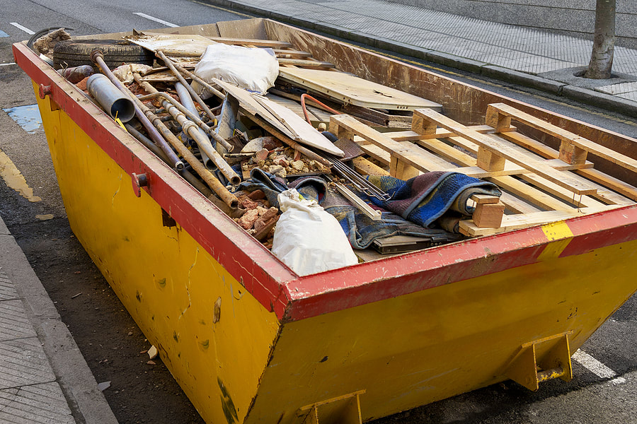 On a White Plains, NY, city road, there is a yellow construction dumpster filled with debris from a house renovation.